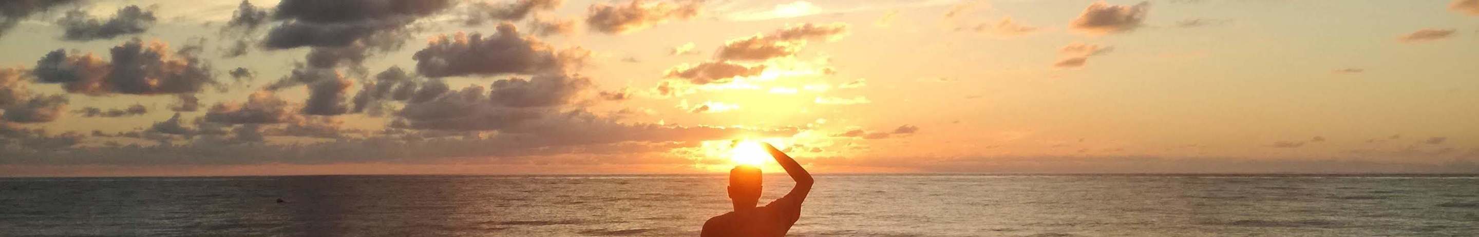 A young man meditating on a beach looking into the sunset.